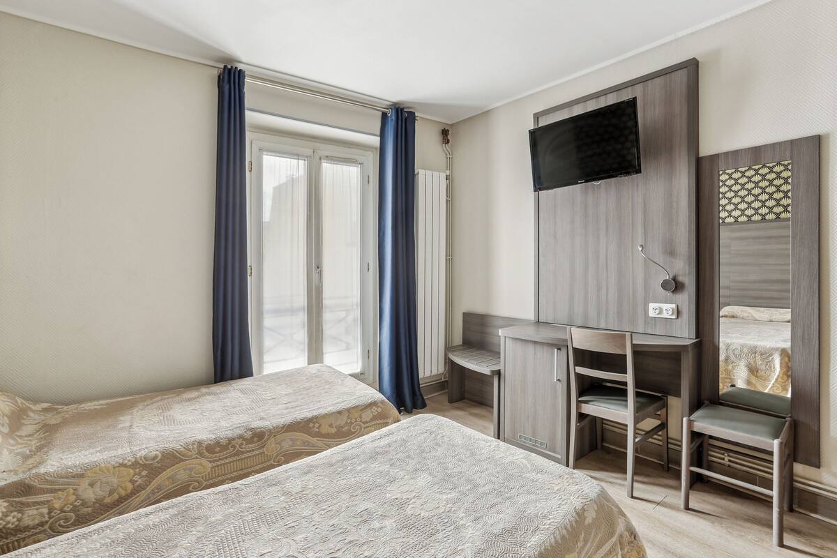 A hotel room with two beds, a desk, a chair, a TV, and a wardrobe.