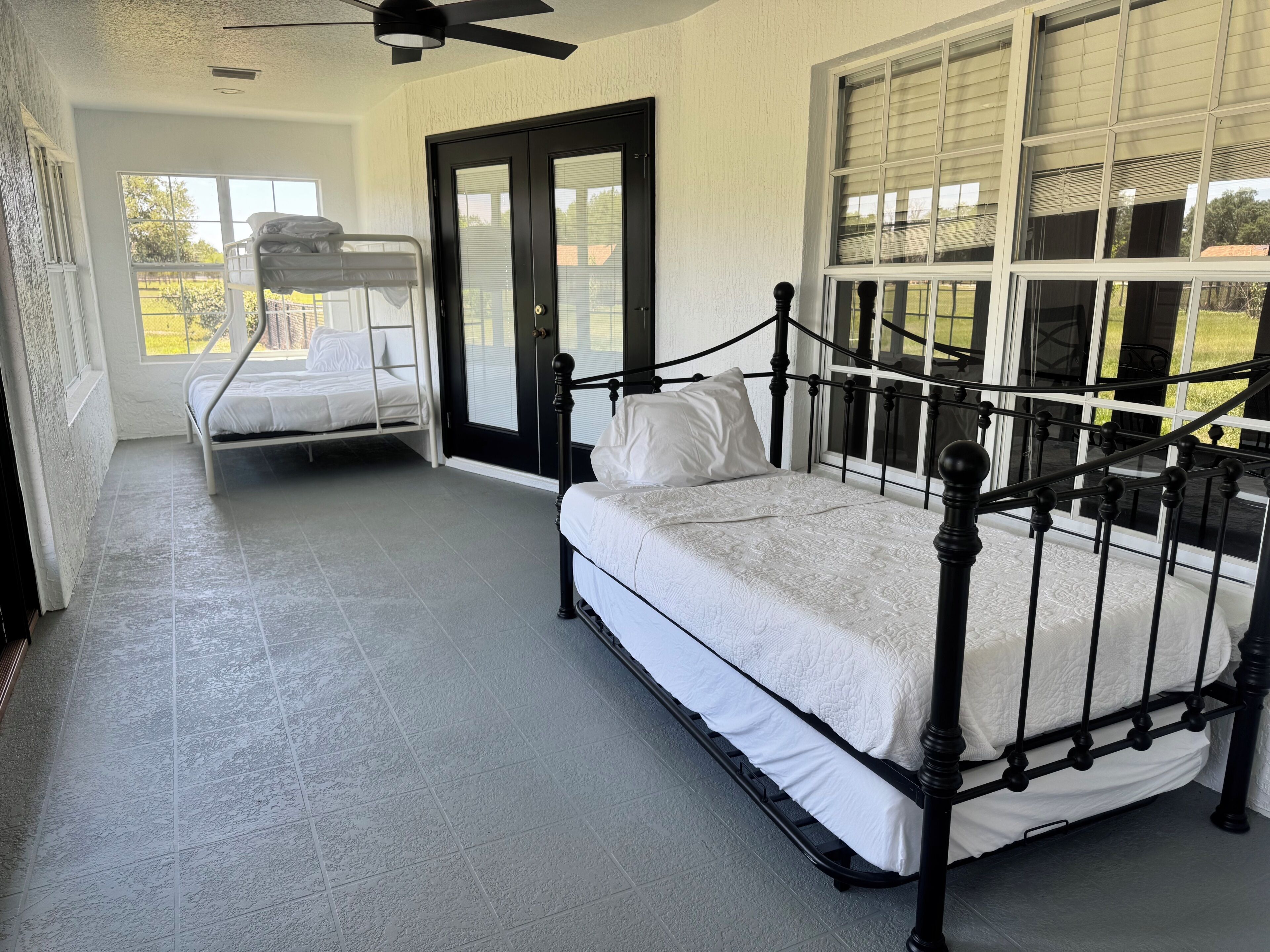 A room with two beds, a ceiling fan, and large windows.