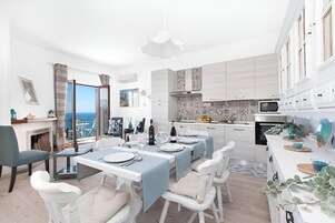 Un comedor moderno con vista al mar, una cocina con armarios blancos y una chimenea.