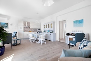 Una cocina moderna con armarios blancos, un comedor con sillas blancas y un piano en la sala.