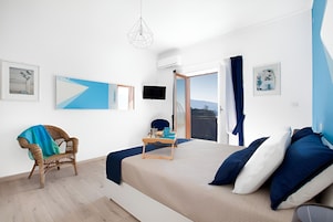 Un dormitorio moderno con una cama, una silla de mimbre, una mesita de noche y vistas a través de un ventanal.