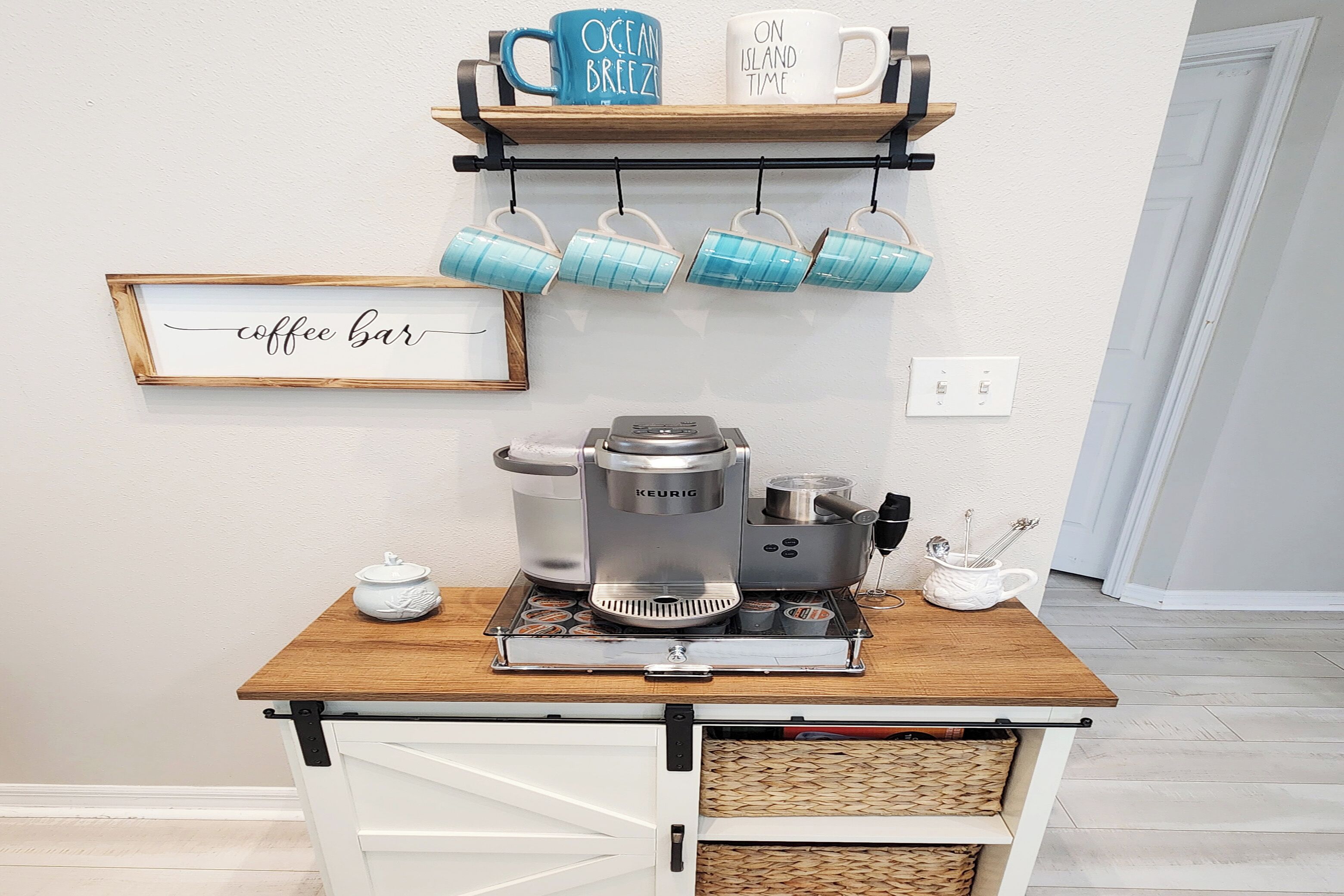A coffee station with a Keurig machine, a coffee pot, and a mug rack with cups.
