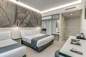 Ein modernes Hotelzimmer mit zwei Betten, einem Schreibtisch mit Kaffeemaschine und einem großen, abstrakten Wandbild.