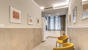 A hallway with two yellow chairs, a kitchen area, and framed artwork on the walls. - Relais Marco Polo (Rome)