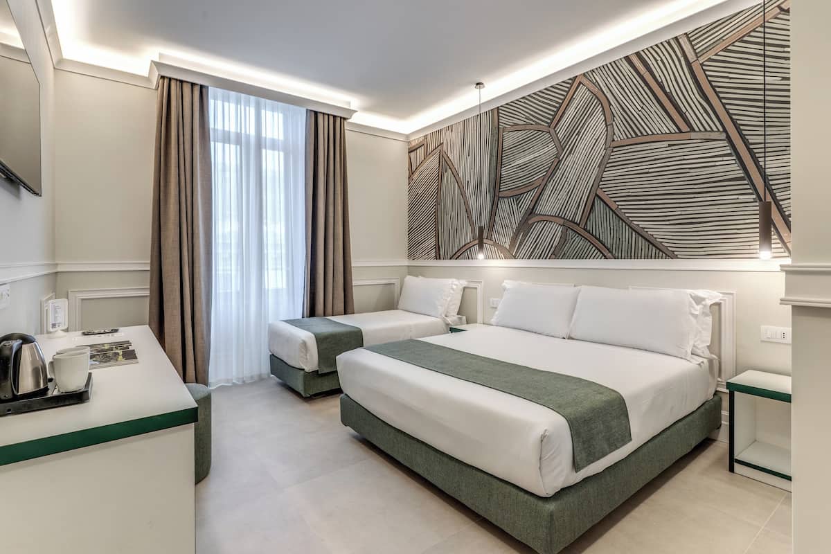 A hotel room with two beds, a desk, and a large wall art piece.
