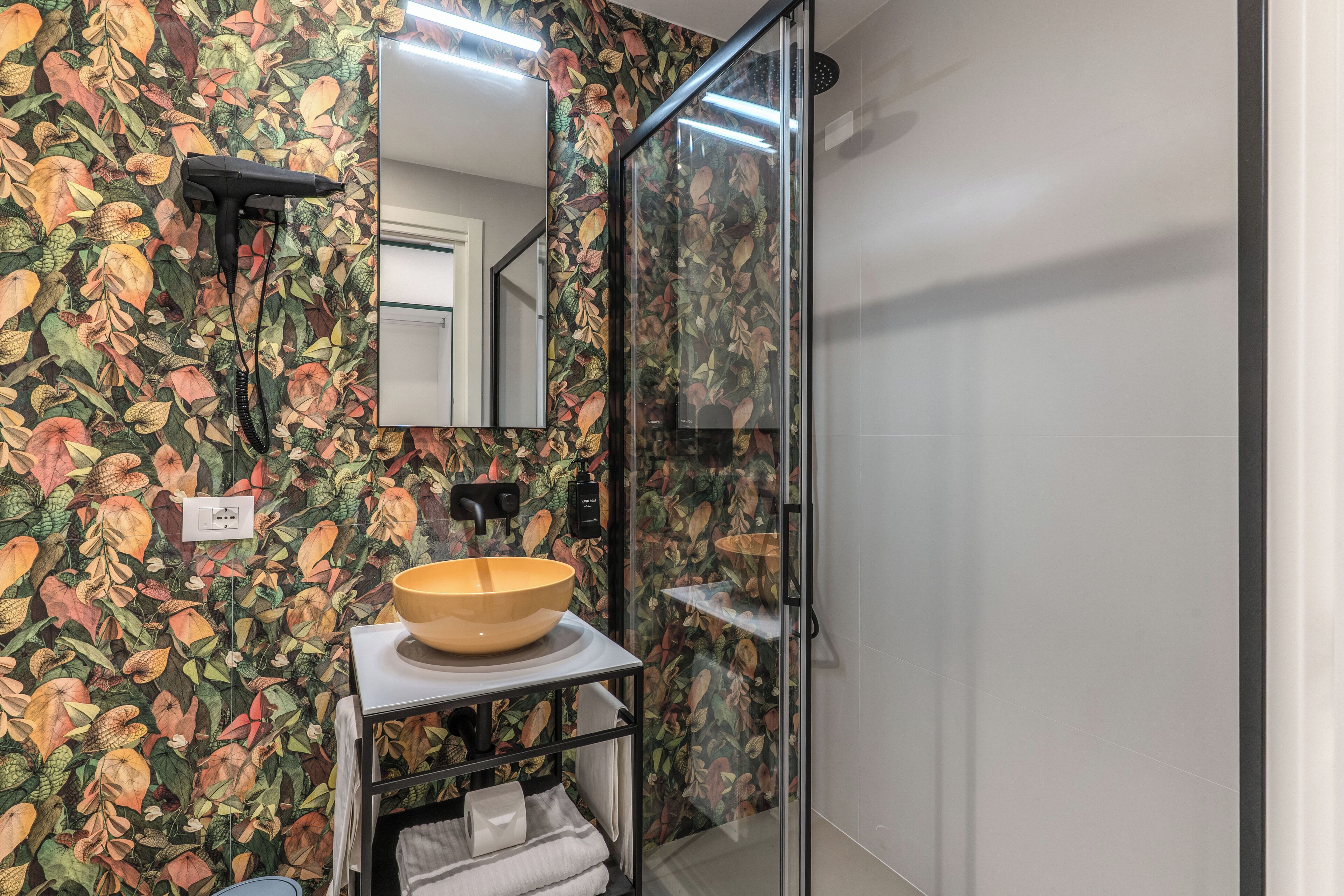 Ein Badezimmer mit floralem Wandpapier, einem Waschbecken aus Holz, einer Duschkabine aus Glas und einem Spiegel über dem Waschbecken.