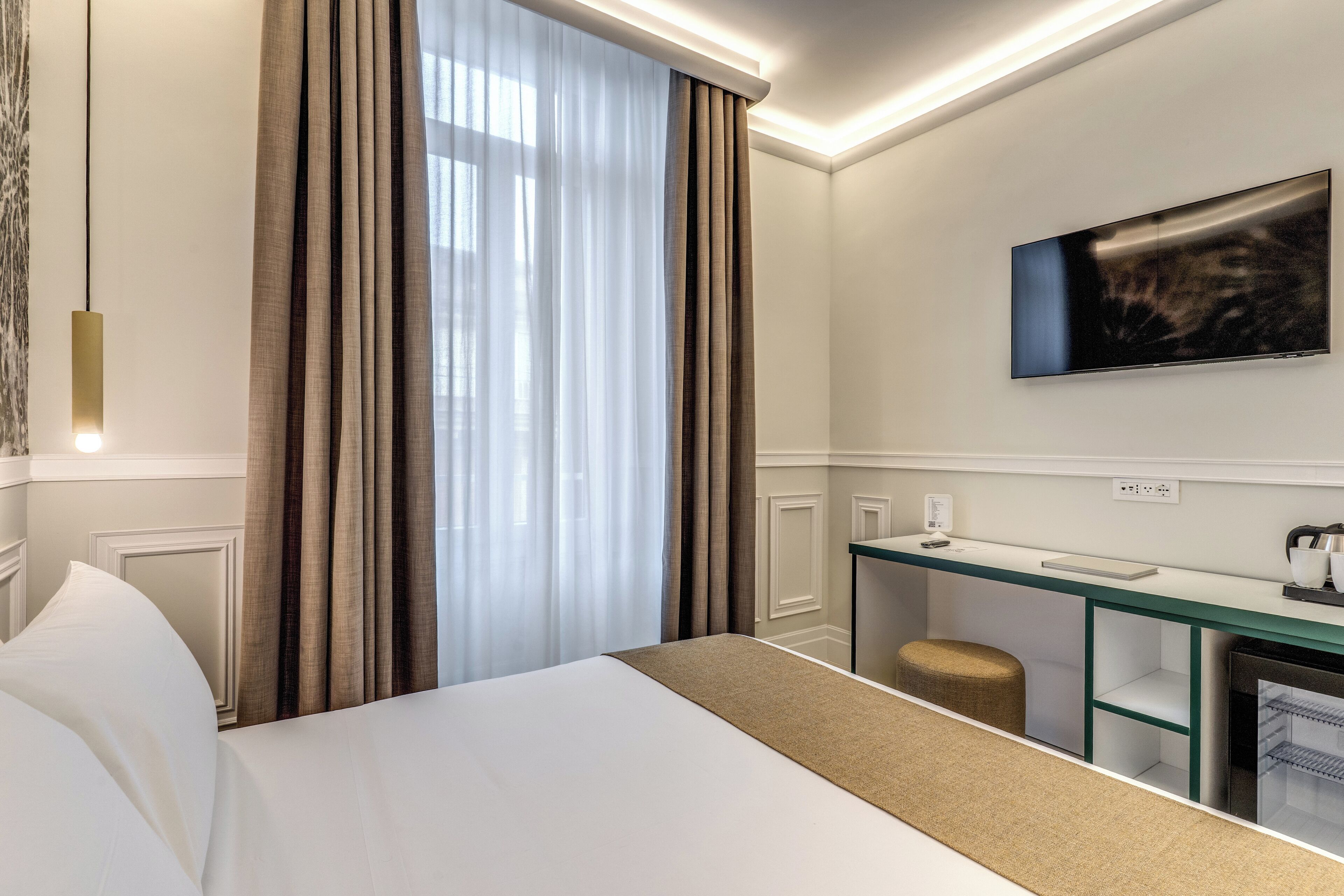 Habitación de hotel con una cama grande, un escritorio con silla, un televisor montado en la pared y una ventana con cortinas.