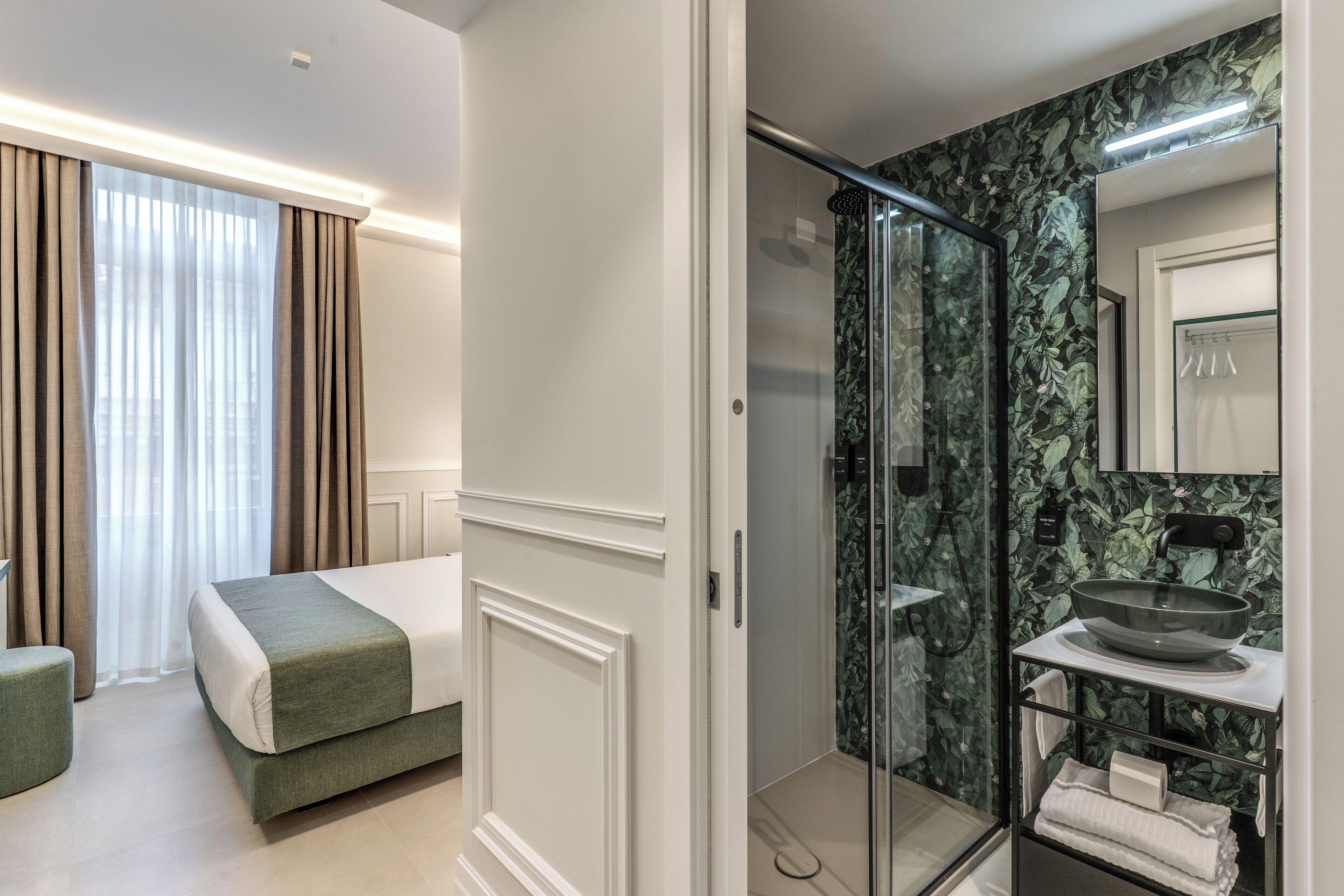 Una habitación de hotel con una cama, ducha con puerta de vidrio y baño con lavamanos y espejo.
