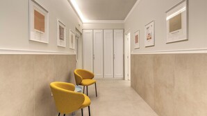 A hallway with two yellow chairs, a white door, and framed pictures on the walls. - Relais Marco Polo (Rome)