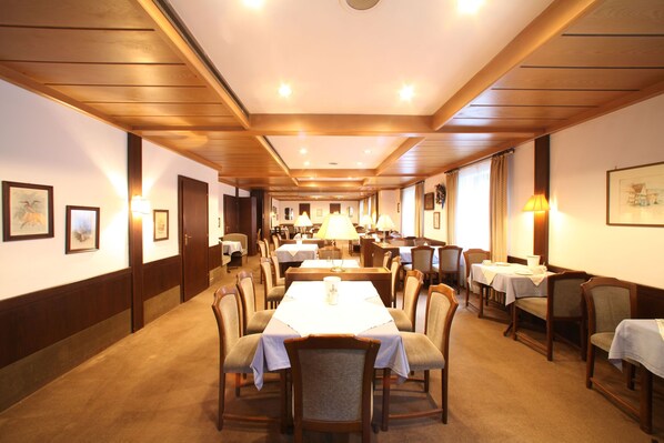 Un comedor de hotel con varias mesas y sillas, paneles de madera en las paredes y cuadros enmarcados.