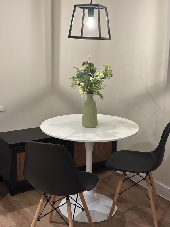 A round table with a white marble top, two black chairs with wooden legs, a green vase with flowers, and a black-framed pendant light. - Renovatedapartmentsleeps4-freeparking-tv (Brentford)