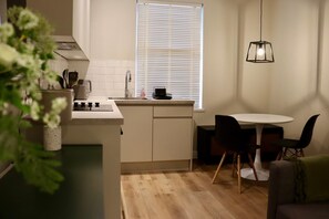 A compact kitchen with a central island, a dining area with a round table and chairs, and a hanging pendant light. - Renovatedapartmentsleeps4-freeparking-tv (Brentford)