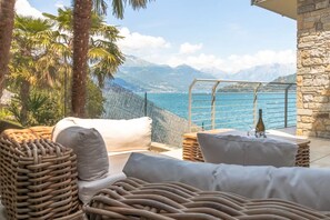 Ein Balkon mit Korbmöbeln, einer Flasche und Blick auf das Meer und die Berge.