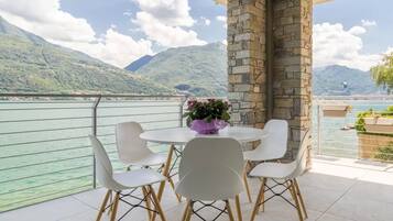 Un balcone con un tavolo rotondo e sedie, affacciato su un lago con montagne sullo sfondo.