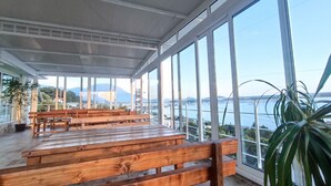 Un espace extérieur abrité, doté de bancs en bois et de grandes fenêtres offrant une vue sur une étendue d’eau et sur des montagnes lointaines.