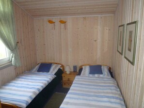 Una habitación pequeña y acogedora con dos camas individuales, piso de madera y una ventana con cortinas.