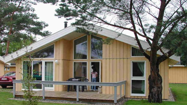 Ein modernes Holzhaus mit Terrasse, großen Fenstern und einem Baum im Garten.
