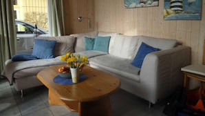Ein gemütliches Wohnzimmer mit einer Couch, einem Couchtisch mit Blumen und zwei Bildern an der Wand.