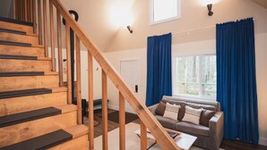 A staircase with wooden steps and a handrail, a living room with a sofa and a coffee table, and a window with blue curtains.
