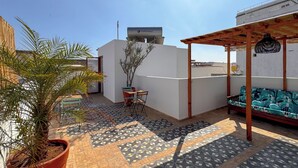 A rooftop patio with a potted palm tree, a small table with chairs, a patterned floor, and a sofa under a wooden pergola. - DAR TAHAR (Rabat)