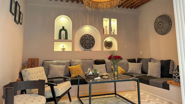 A modern living room with a sofa, armchairs, and a coffee table. There are decorative wall sconces and a chandelier. - DAR TAHAR (Rabat)