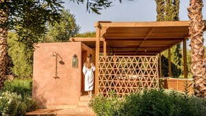Une structure en bois dotée d’un mur en treillis et d’une petite porte, entourée de verdure et d’arbres.