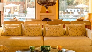 Un coin salon accueillant, avec un canapé agrémenté de coussins à motifs, un luminaire décoratif suspendu et une table ornée de verres verts et oranges.