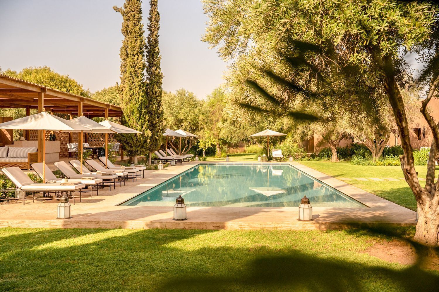 Zona de piscina amb gandules, ombrelles i una pèrgola.