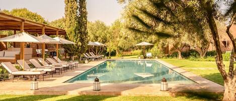 Zona de piscina amb gandules, ombrelles i una pèrgola.