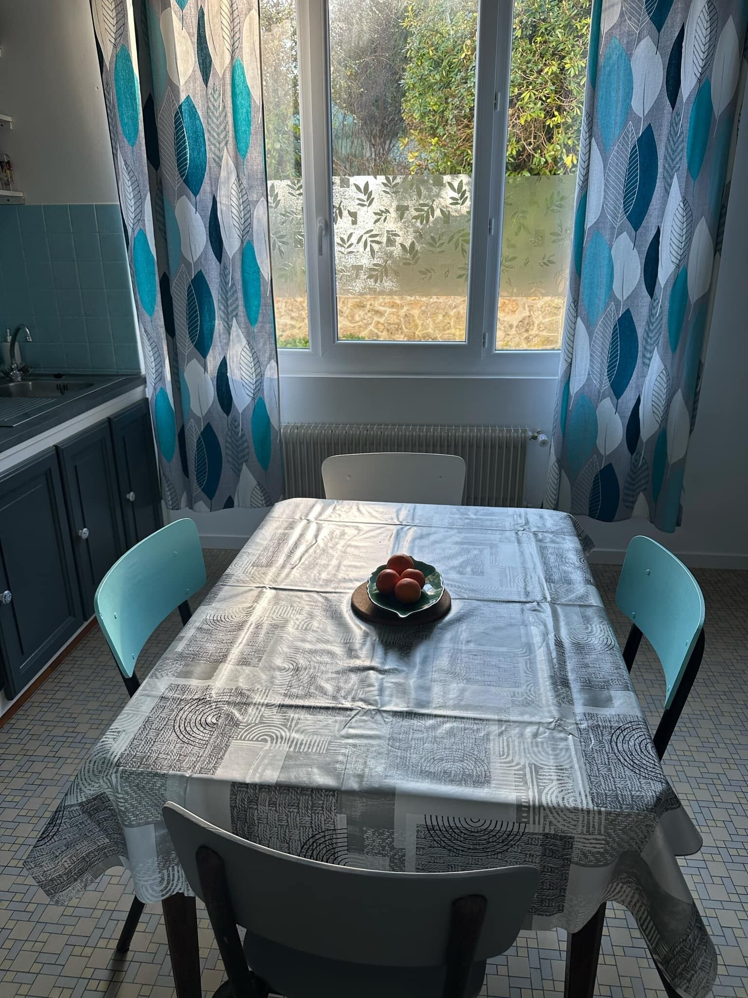Een eetgedeelte met een tafel voor vier personen, een fruitschaal en uitzicht op de tuin door een raam.
