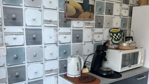 Et køkken med en hvid og grå ternet bagplade, et billede af to kvinder, en elkedel, en mikrobølgeovn og en skraldespand.