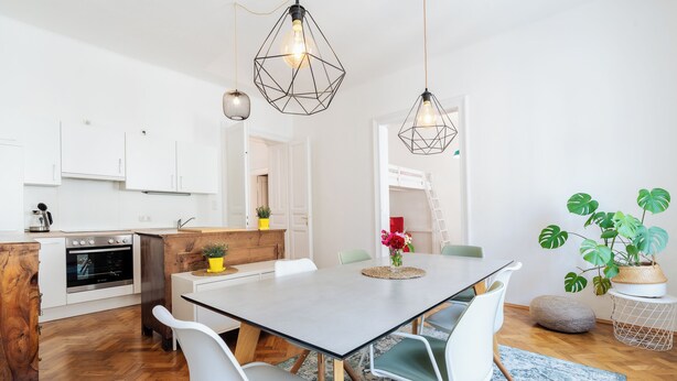 Une cuisine moderne avec des armoires blanches, un comptoir en bois et un four encastré. On y trouve également un coin repas avec une table, des chaises et des luminaires suspendus.
