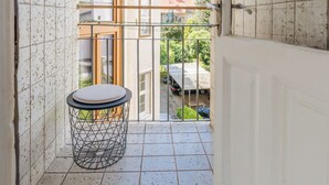 Un balcon étroit doté d’un sol carrelé, d’une petite table ronde et d’un panier en métal.