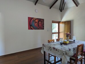 Un coin repas avec une table dressée pour deux personnes, un tableau au mur et une fenêtre donnant sur un paysage verdoyant.