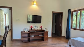 A room with a wooden floor, a bed, a TV mounted on the wall, and a wooden cabinet with decorative plates. - Villa #248 (Somvarpet)