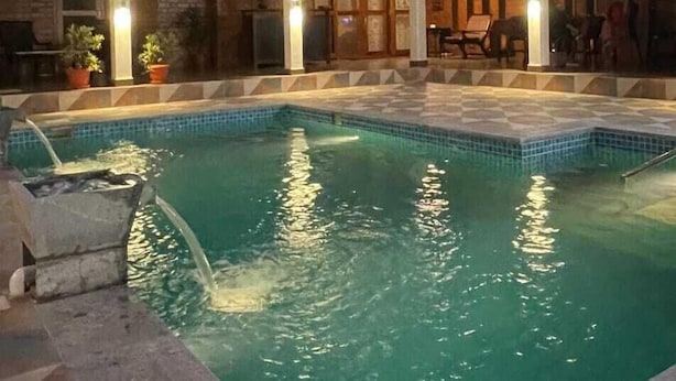 A swimming pool with a tiled deck, surrounded by a building with multiple windows and a covered patio area. - Villa #248 (Somvarpet)