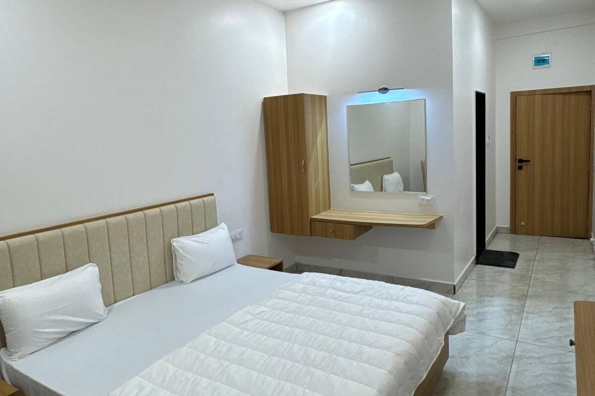 A modern bedroom with a large bed, a wooden wardrobe, a bedside table, a mirror, and a ceiling fan.