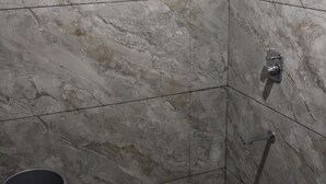A shower area with a handheld showerhead, a wall-mounted faucet, and a floor drain.