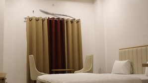 A hotel room with a bed, two chairs, a small table, and a curtain.
