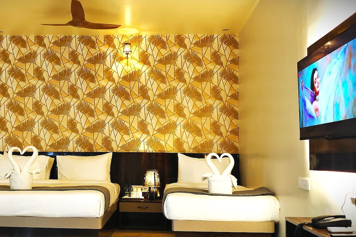 A hotel room with two beds, a ceiling fan, a TV, and a patterned wall.