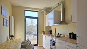 A modern kitchen with a dining area, featuring a large window, stainless steel appliances, and a wooden table. - Apartments am Immengarten (Hannover)