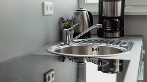 A stainless steel kitchen sink with a modern faucet, a coffee maker, and a small potted plant on the countertop. - Apartments am Immengarten (Hannover)