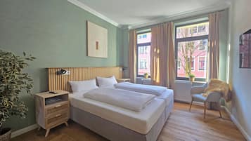Quarto de hotel com uma cama grande, mesa de cabeceira, uma cadeira e vista para o exterior.