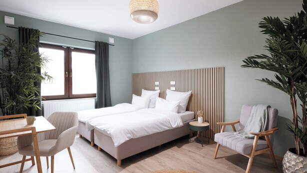 A modern bedroom with a large bed, a desk, two chairs, and a potted plant. - Apartments am Immengarten (Hannover)