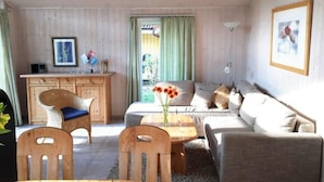 A cozy living room with a wooden ceiling, a sofa set, a dining table with chairs, and a kitchen area with a cabinet and a framed picture on the wall. - Ferienhaus mit Sauna im Ferienpark Mirow (Mirow)