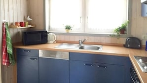 A compact kitchen with a microwave, kettle, sink, and dishwasher. There is a window with a view of the outdoors. - Ferienhaus mit Sauna im Ferienpark Mirow (Mirow)