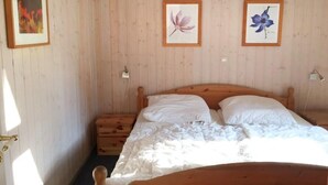A bedroom with a wooden bed, a nightstand, and two framed floral pictures on the wall. - Ferienhaus mit Sauna im Ferienpark Mirow (Mirow)