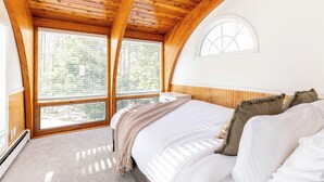 Een slaapkamer met een houten plafond, een groot raam en een bed met wit beddengoed.