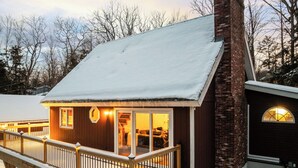 Een houten chalet met terras, een bakstenen schoorsteen en een aangebouwde garage.