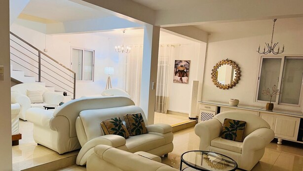 A modern living room with a sofa set, a glass coffee table, and a dining area with a chandelier. - Salty Chateau: Private Exquisite Mauritian Getaway (Cap Malheureux)